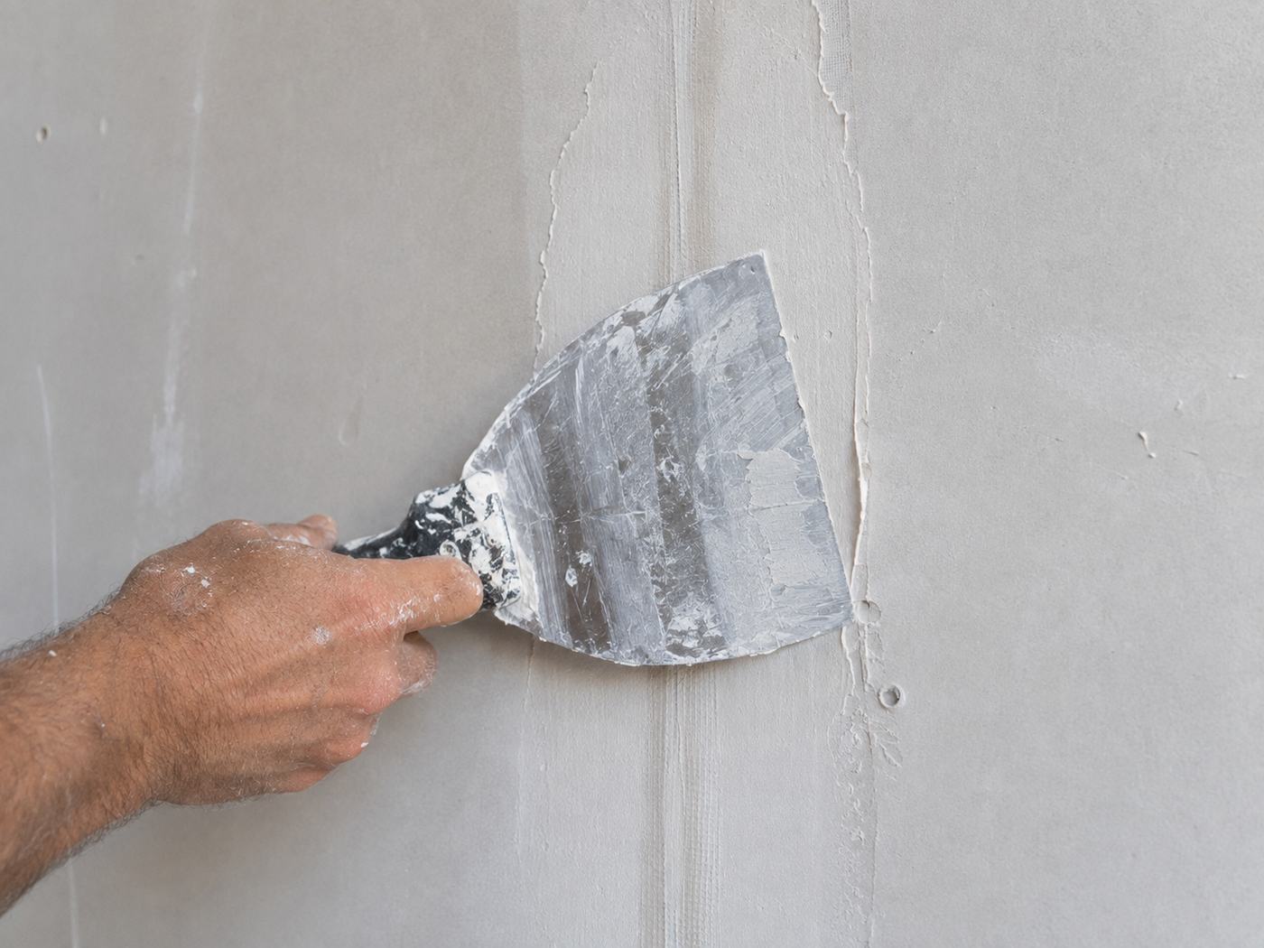 Close-up of skim coating a wall with a putty knife